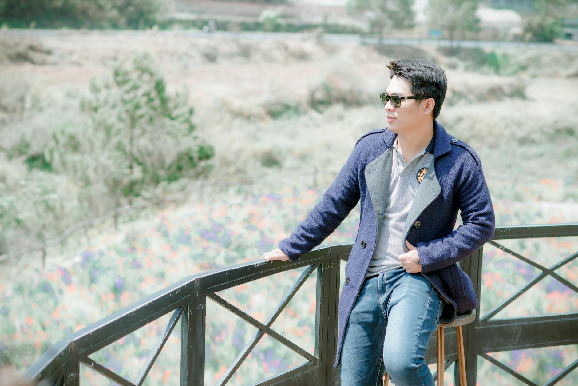Young man in sunglasses sitting casually on a balcony railing.