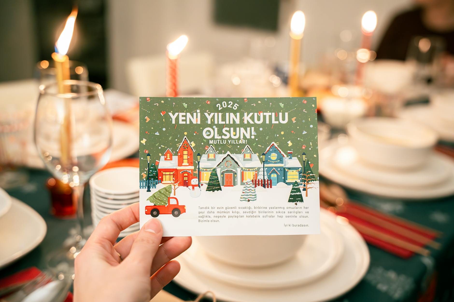 A hand holding a 2025 New Year's greeting card over a festive dinner table set for celebration.