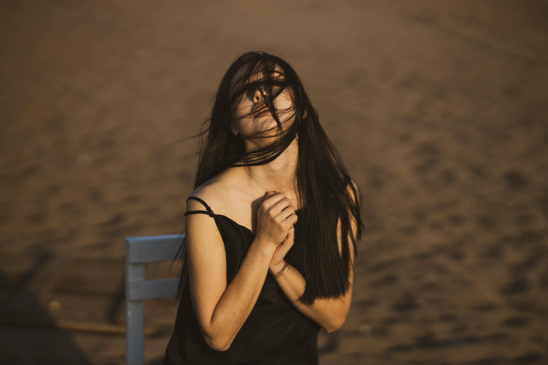 A woman with long hair poses in a windy setting on a sandy beach, exuding elegance and emotion.
