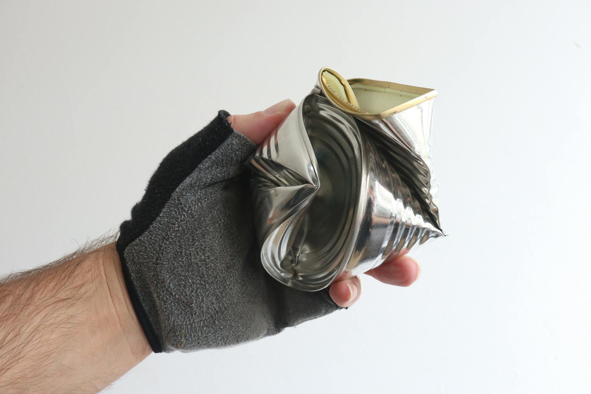 A gloved hand holding a crushed tin can showcases recycling and waste management.