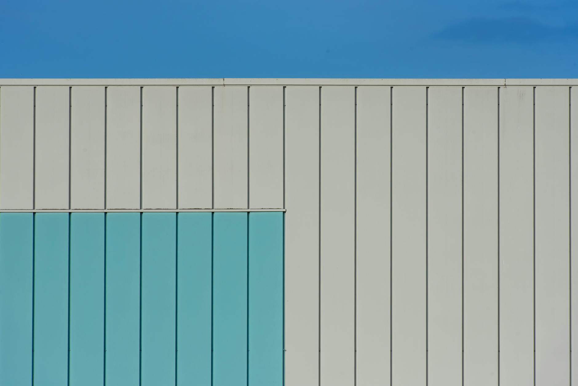 Abstract view of a modern building facade with geometric design and blue accents under a clear sky.