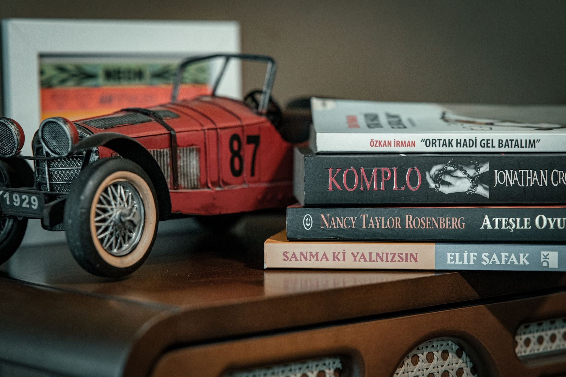 Vintage model car with stacked books on wooden table in a cozy room.