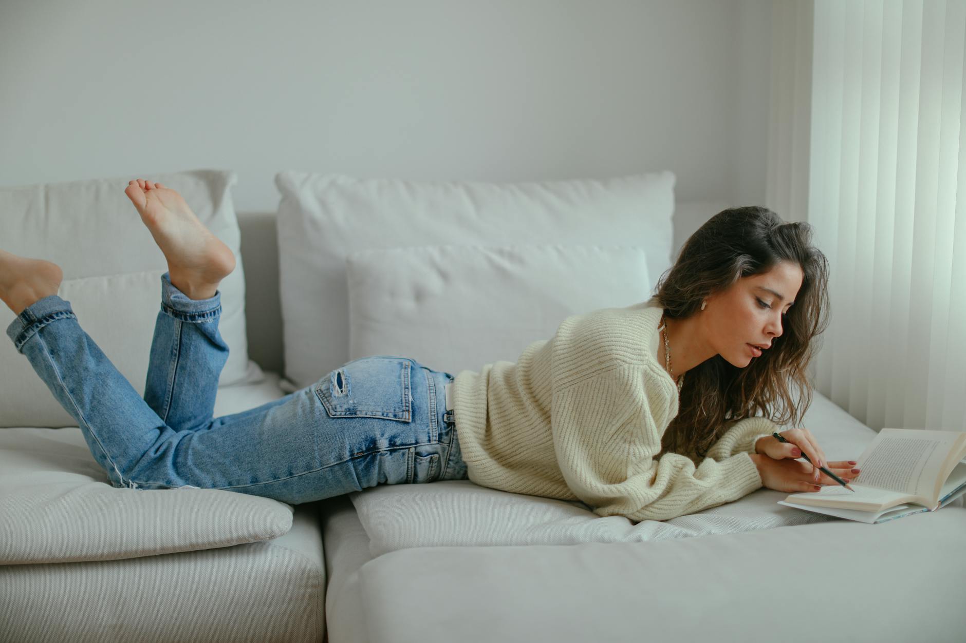 A young woman in casual attire enjoys a book while relaxing on a comfortable sofa indoors.