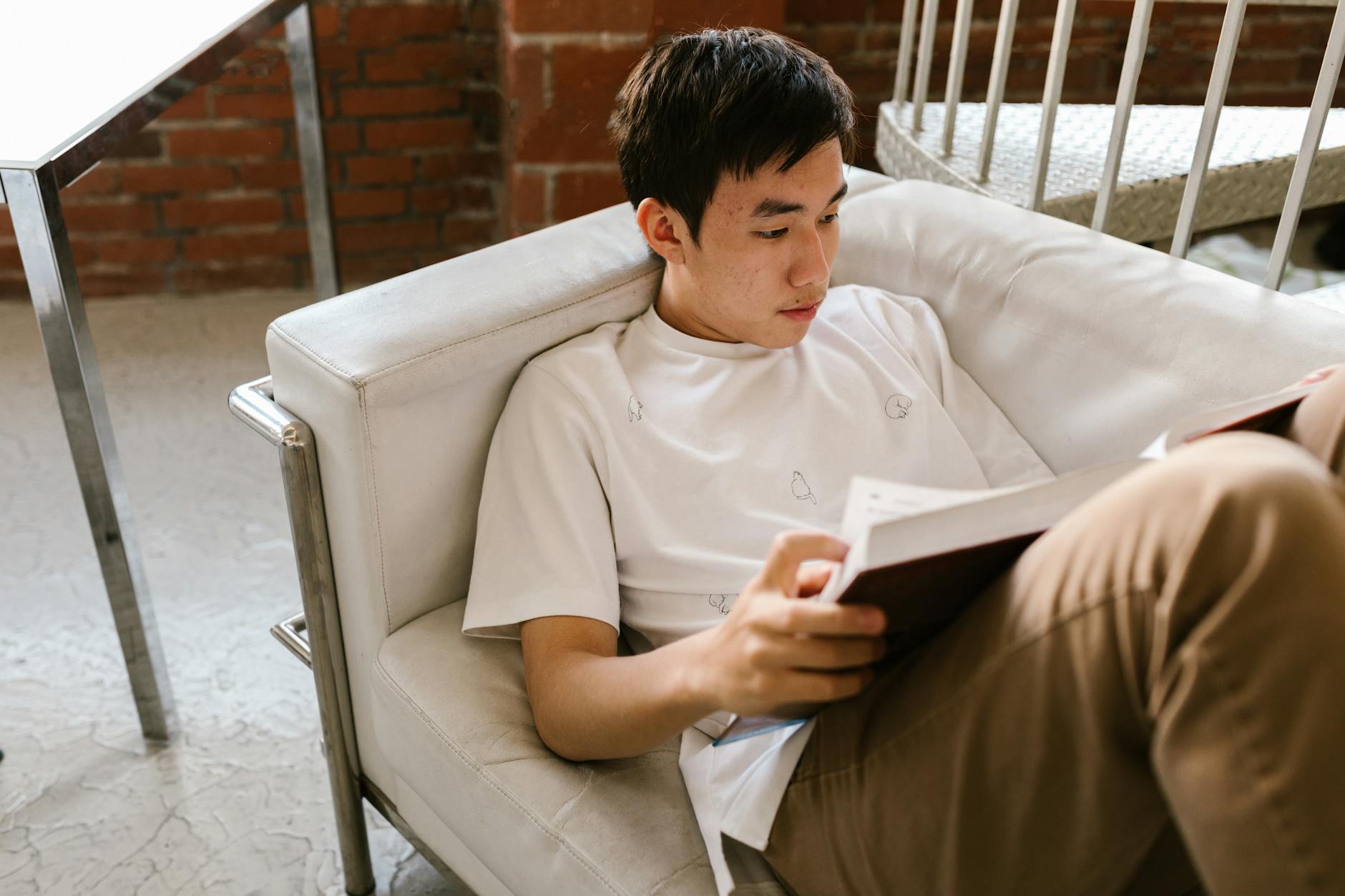 A teenager reading a book while lounging on a sofa in a cozy indoor setting.