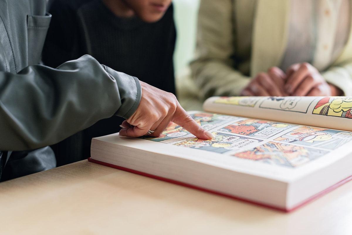 Two individuals focus on reading a colorful comic book, highlighting engaging stories.