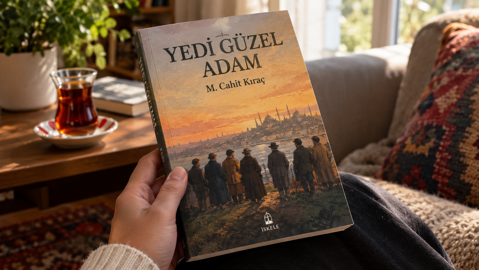 Yedi Guzel Adam kitabini tutan bir el, sicak bir oturma odasinda cay bardagi