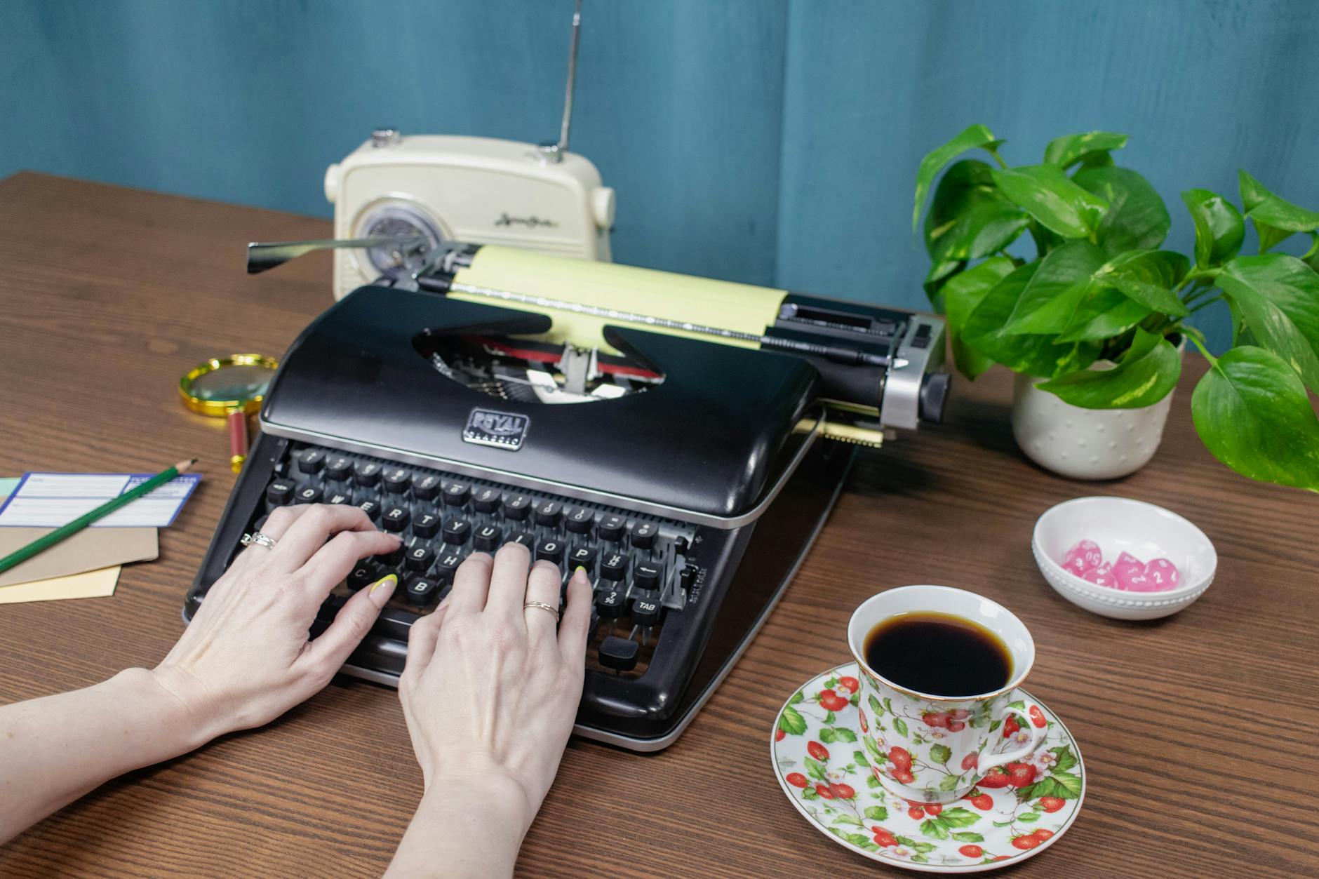 Hands typing on a vintage typewriter with coffee and plants nearby. Retro office setting.