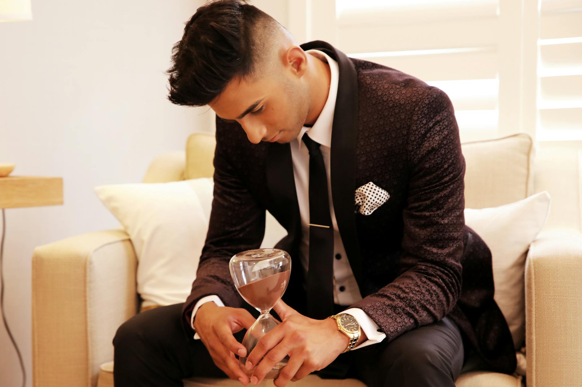 Man in a formal suit holds hourglass, symbolizing time and contemplation.