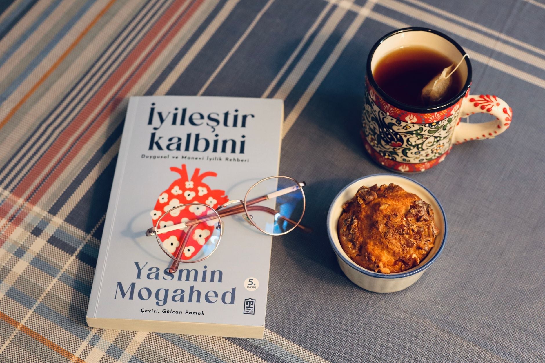 A cozy setting with a book, tea, and muffin on a plaid surface for a relaxing vibe.