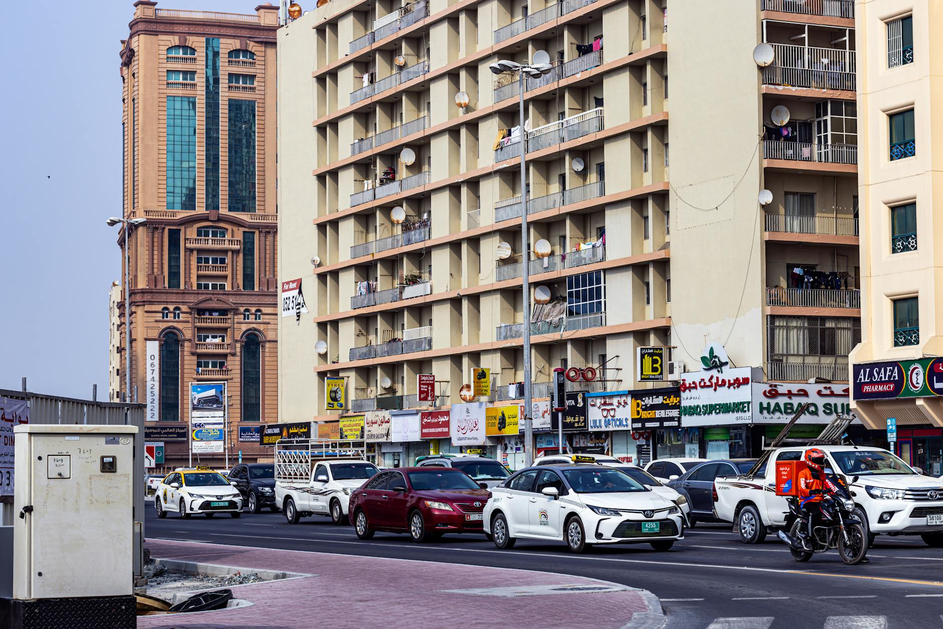 Lively urban street in Dubai featuring cars, motorbikes, and high-rise buildings on a sunny day.