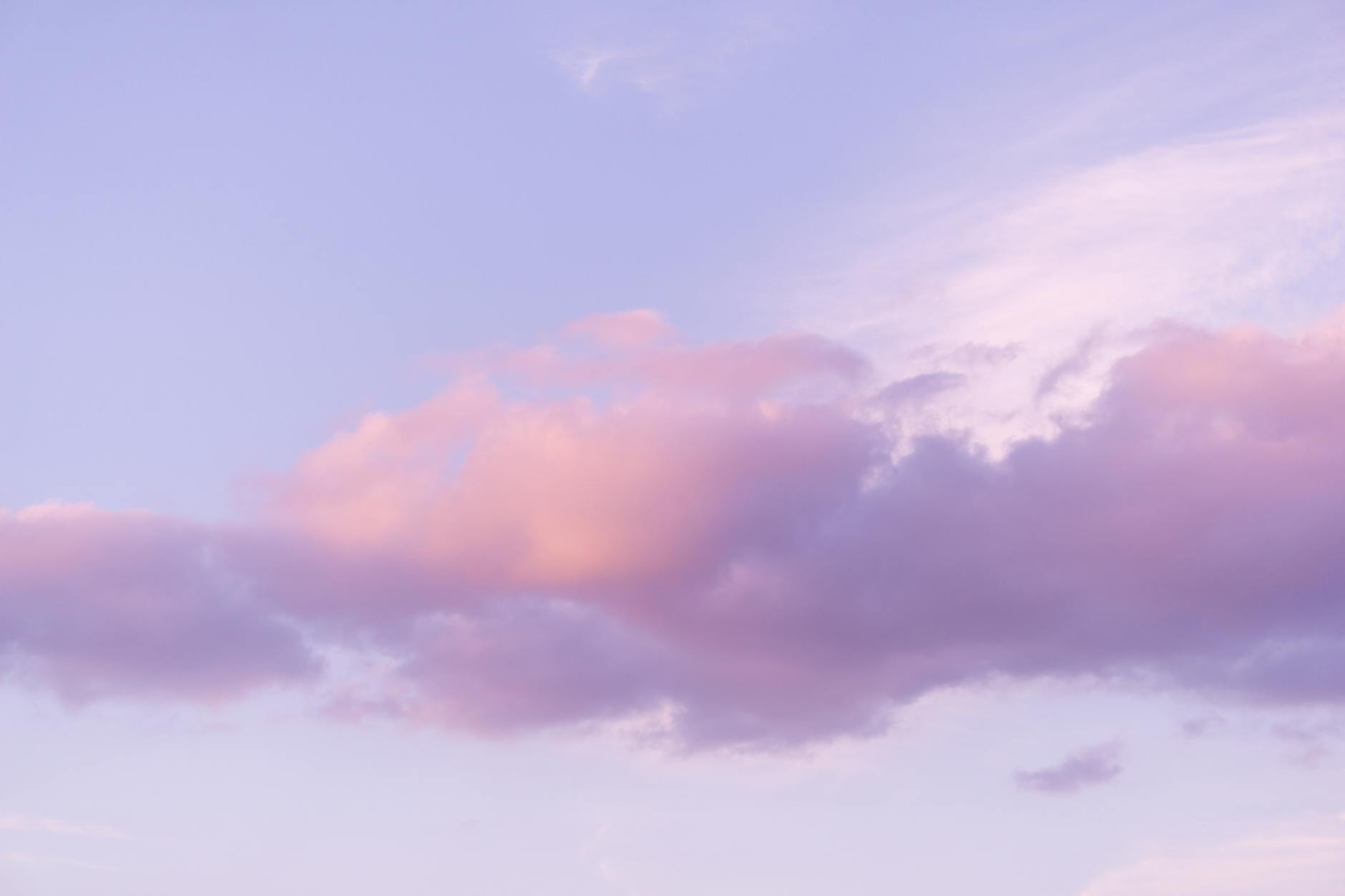 A calming view of pink and purple clouds floating in a clear sky during sunset.